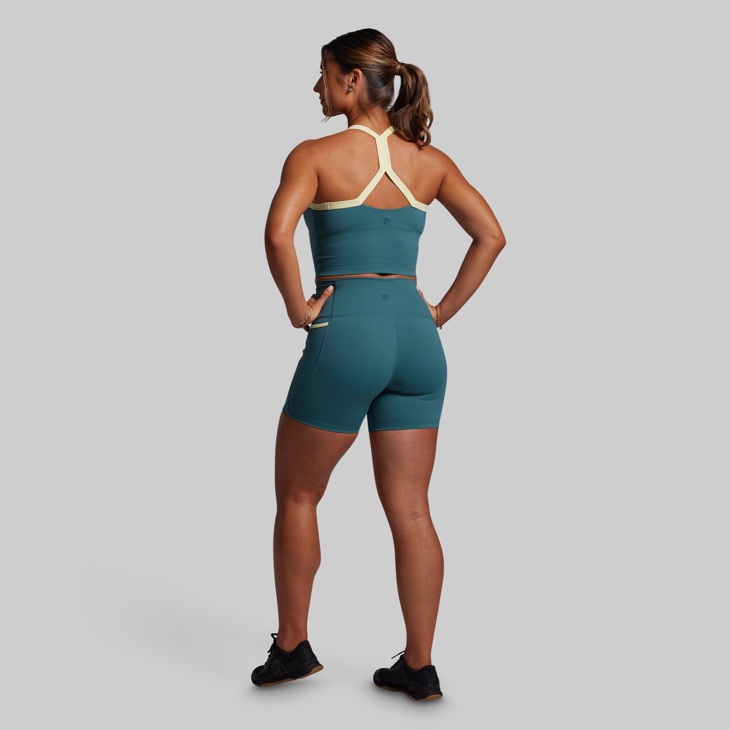 Woman wearing a green sports bra and shorts on a gray background