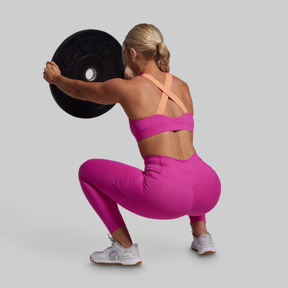 Woman in pink athletic wear lifting a weight plate on a gray background
