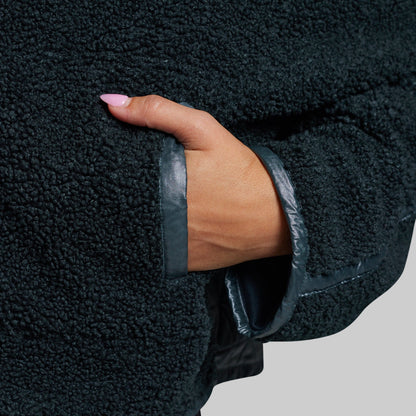 Close-up of a person's hand tucked into a sherpa fleece jacket pocket, showing a faux-leather cuff.