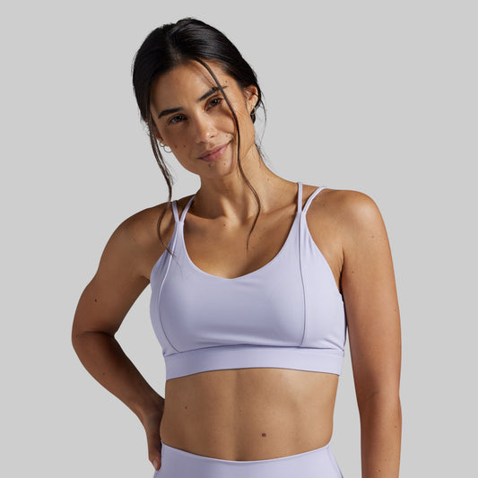 A woman modeling a light lavender sports bra against a solid gray studio background.