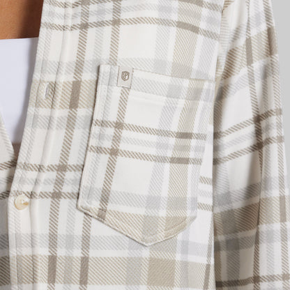 Close-up of a plaid button-up shirt with a chest pocket, featuring a cream and beige pattern with a small logo patch on the pocket.
