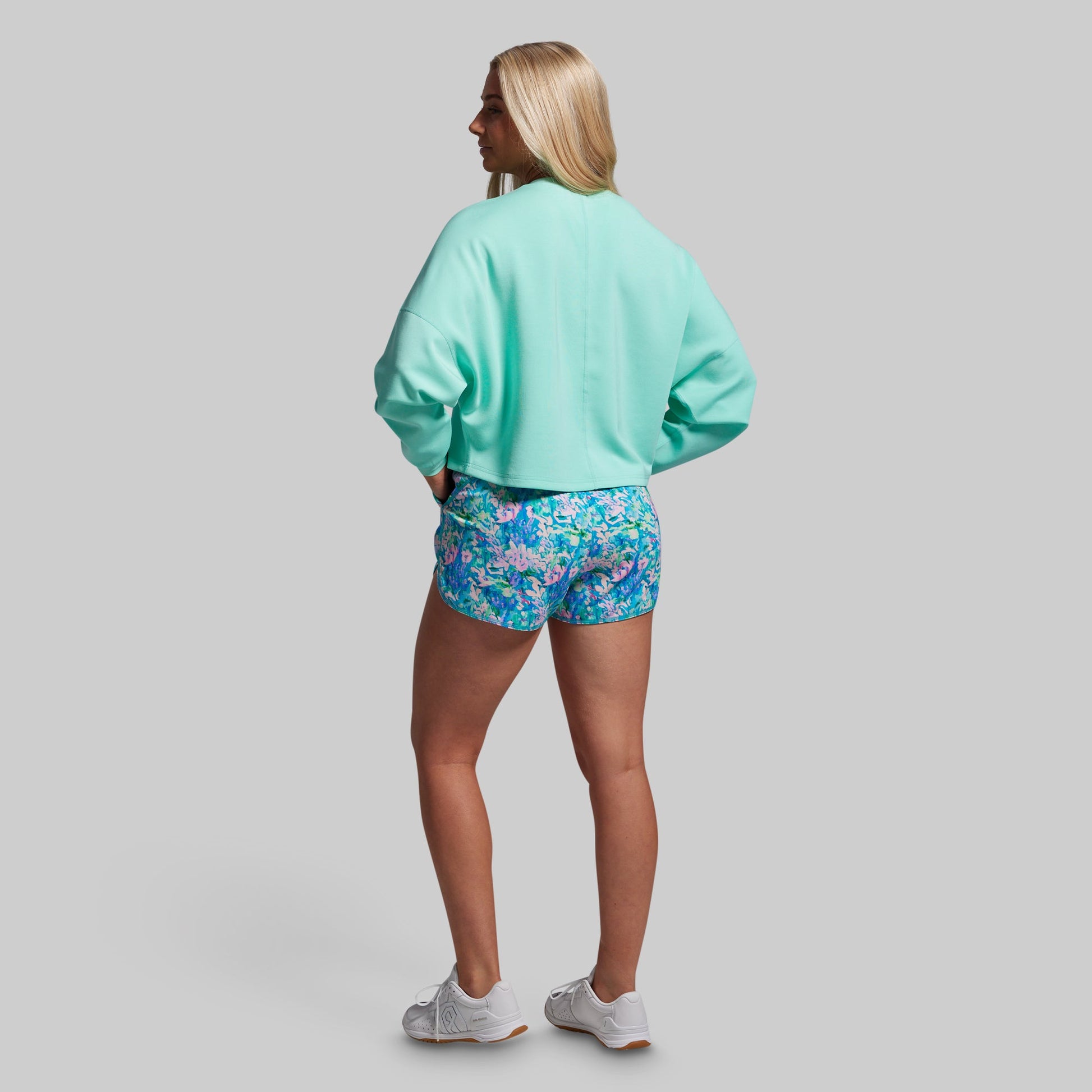 Person wearing a light blue sweatshirt and floral shorts on a gray background
