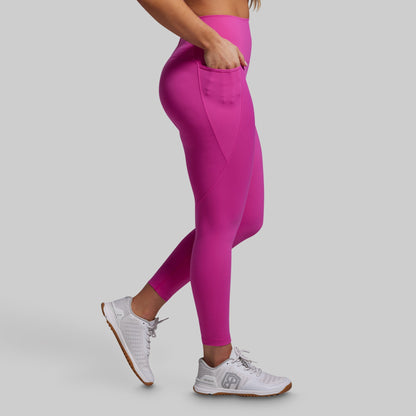 Person wearing bright pink leggings with pockets and white sneakers on a gray background