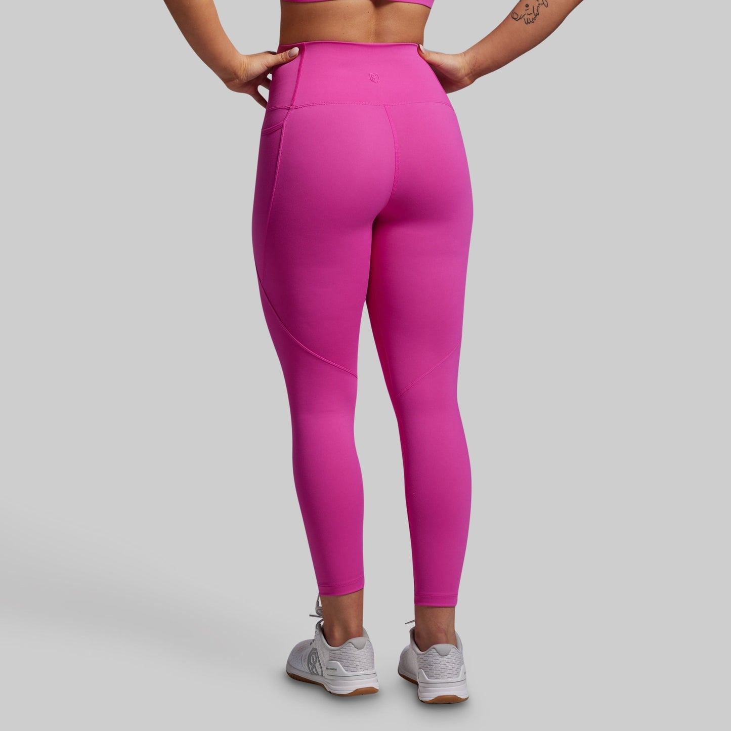 Person wearing bright pink leggings with pockets on a gray background