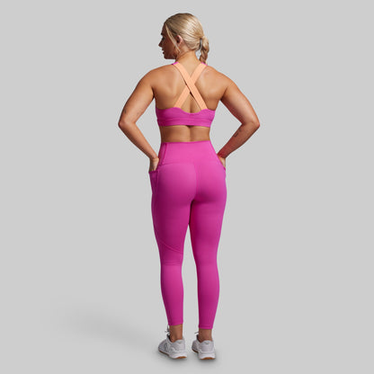 Woman wearing a pink sports bra and leggings with pockets set on a gray background