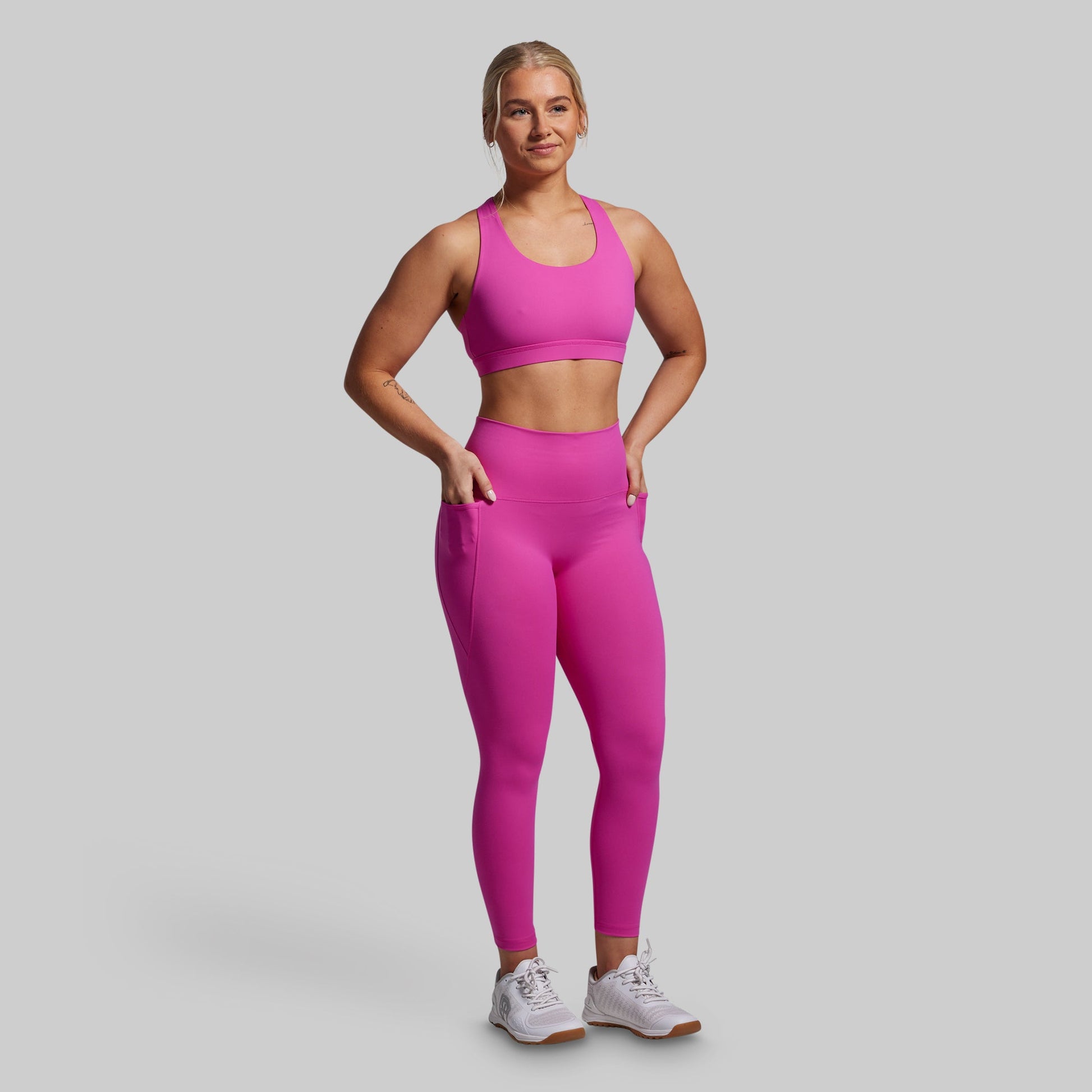 Woman wearing a pink sports bra and leggings with pockets set on a gray background