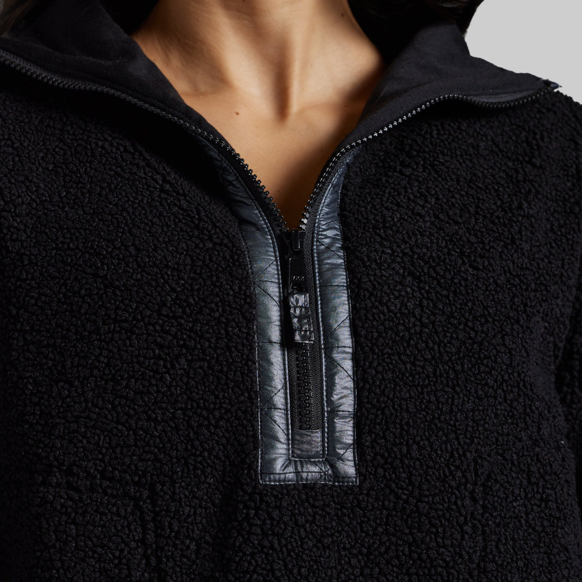 Close-up of a person wearing a black sherpa fleece quarter-zip pullover with a contrasting black faux-leather placket and zipper trim.