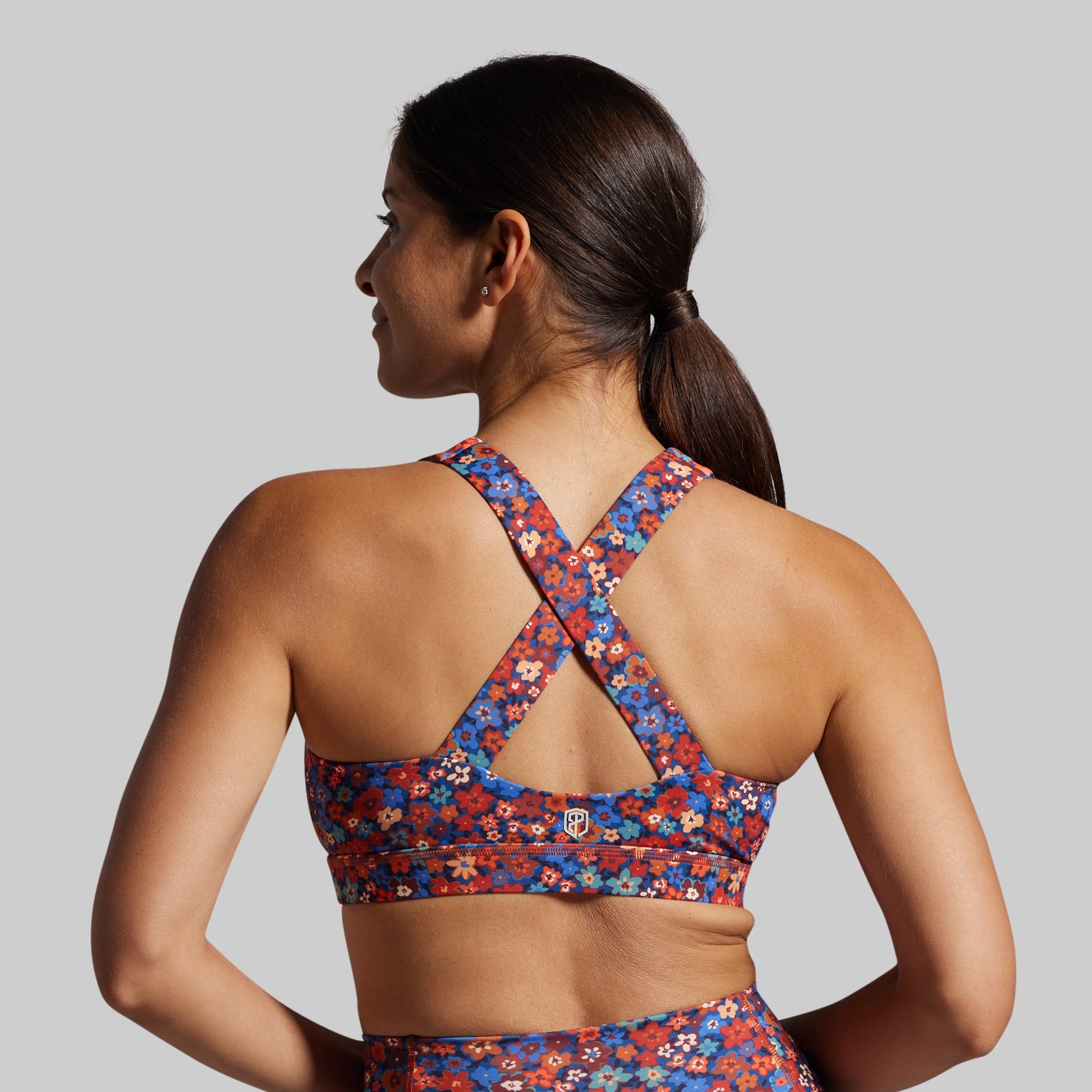 Woman wearing a colorful floral sports bra and shorts on a gray background