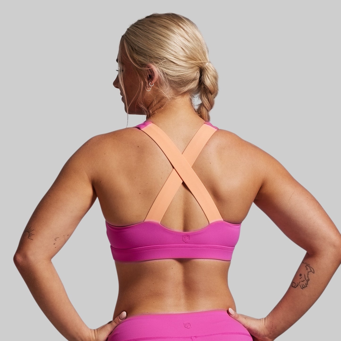 Woman wearing a pink sports bra and leggings on a gray background