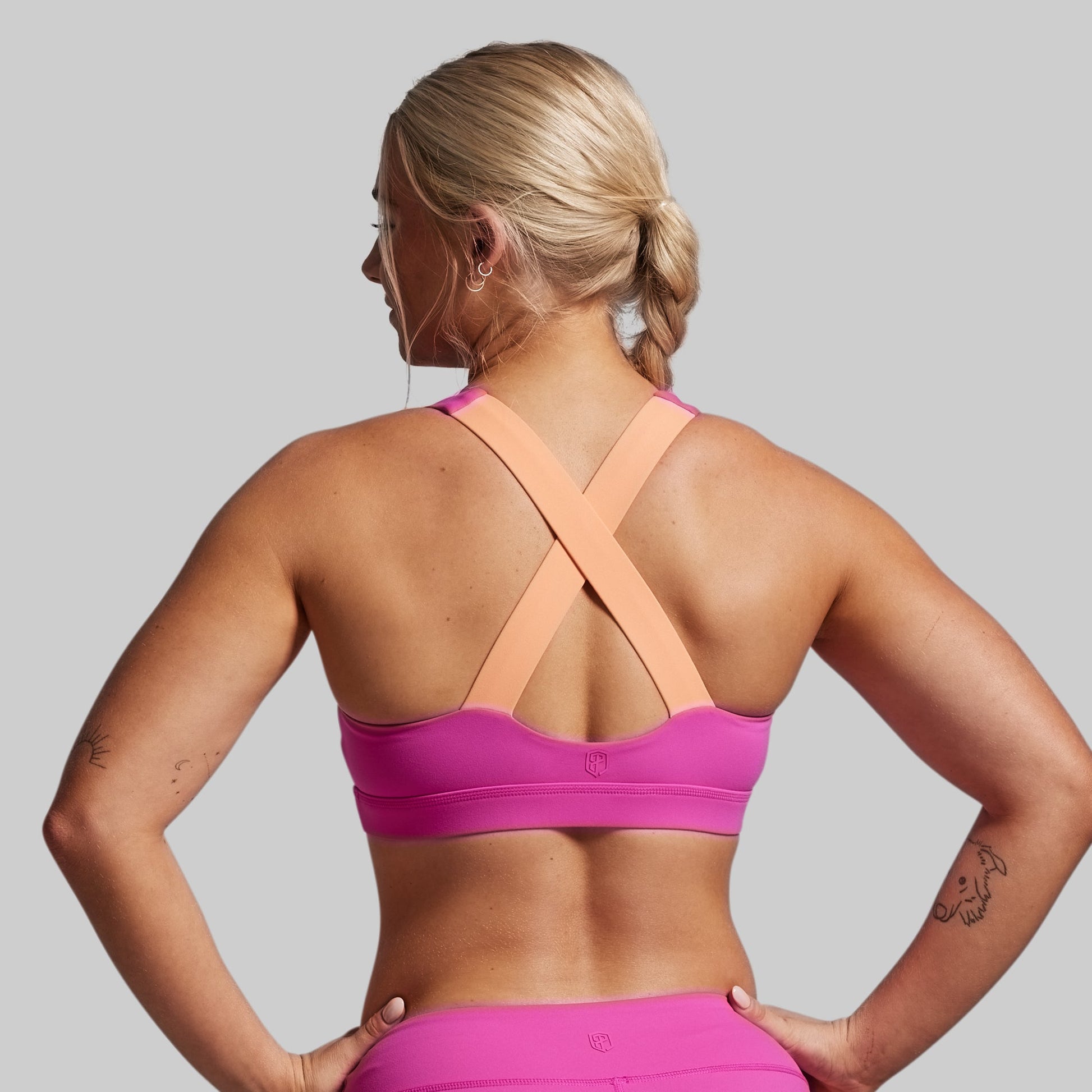 Woman wearing a pink sports bra and leggings on a gray background