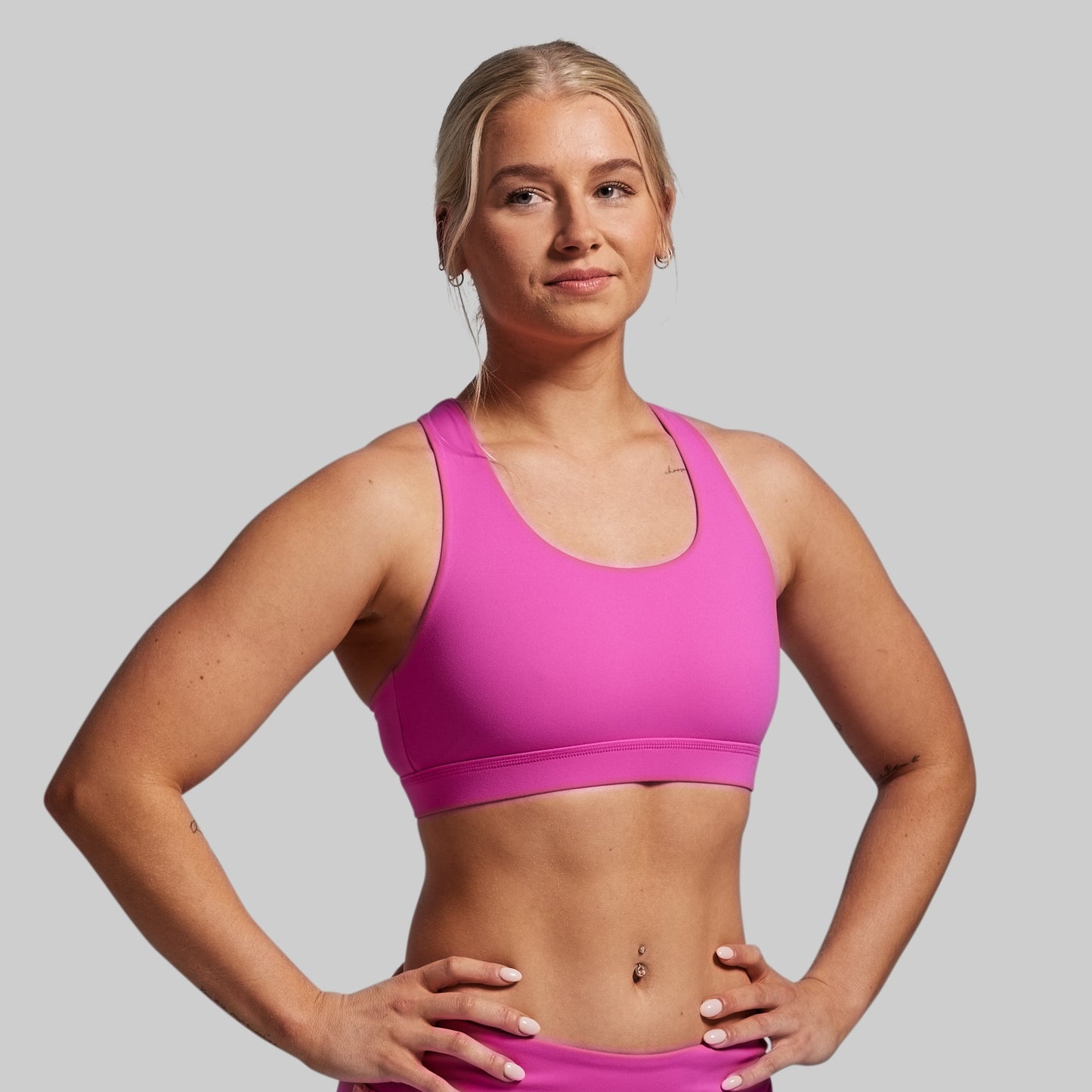 Woman wearing a pink sports bra and shorts on a gray background