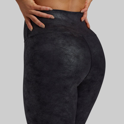 Close-up back view of a person wearing dark charcoal high-waisted leggings against a light gray studio background.