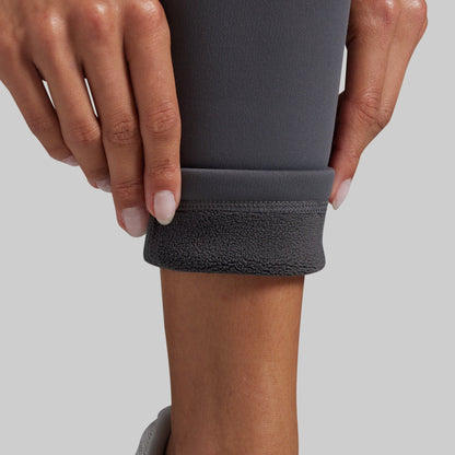 Close-up of a person's hands and lower leg pulling up the cuff of dark gray leggings to reveal a soft, fleece-lined interior.