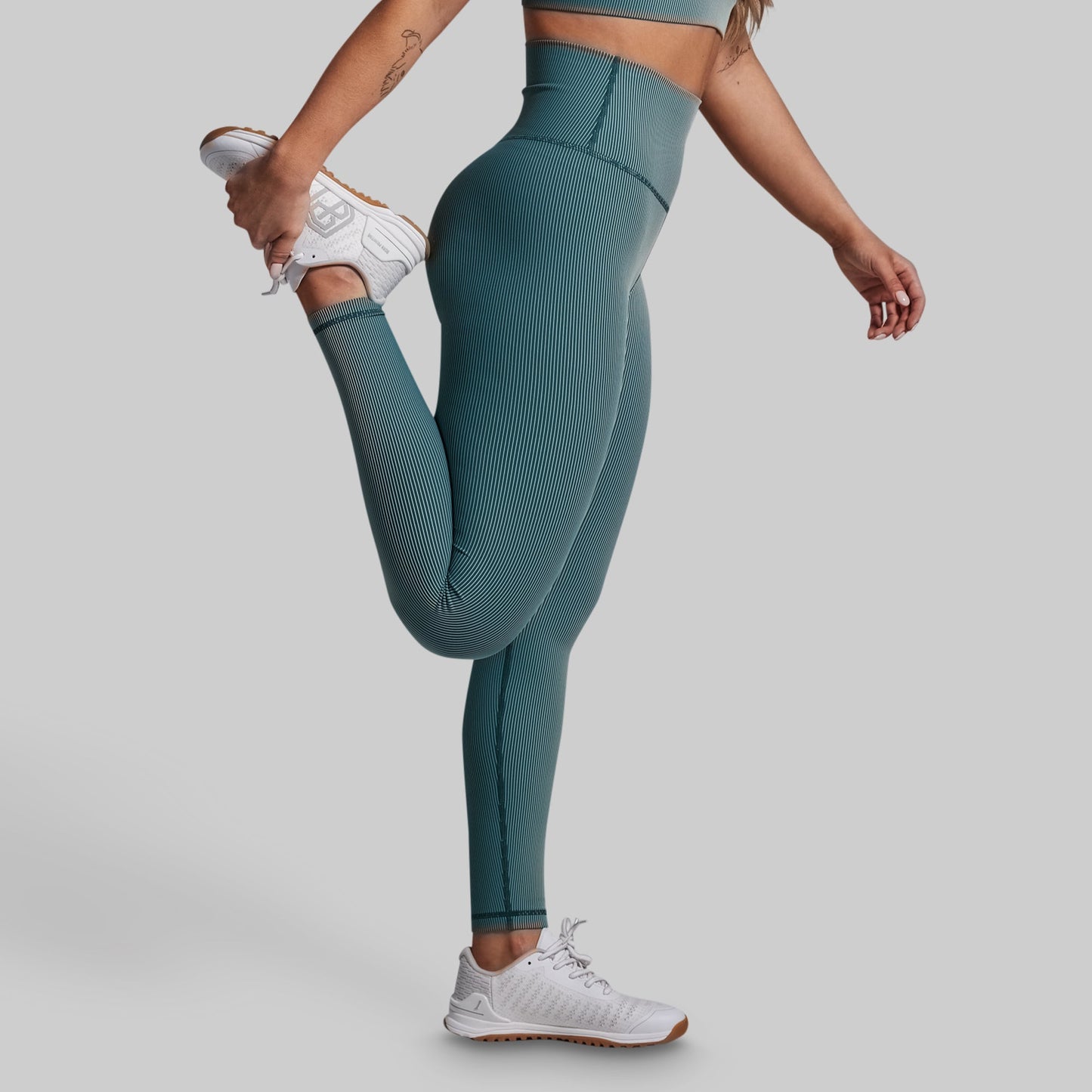 Person wearing teal leggings and white sneakers on a plain background
