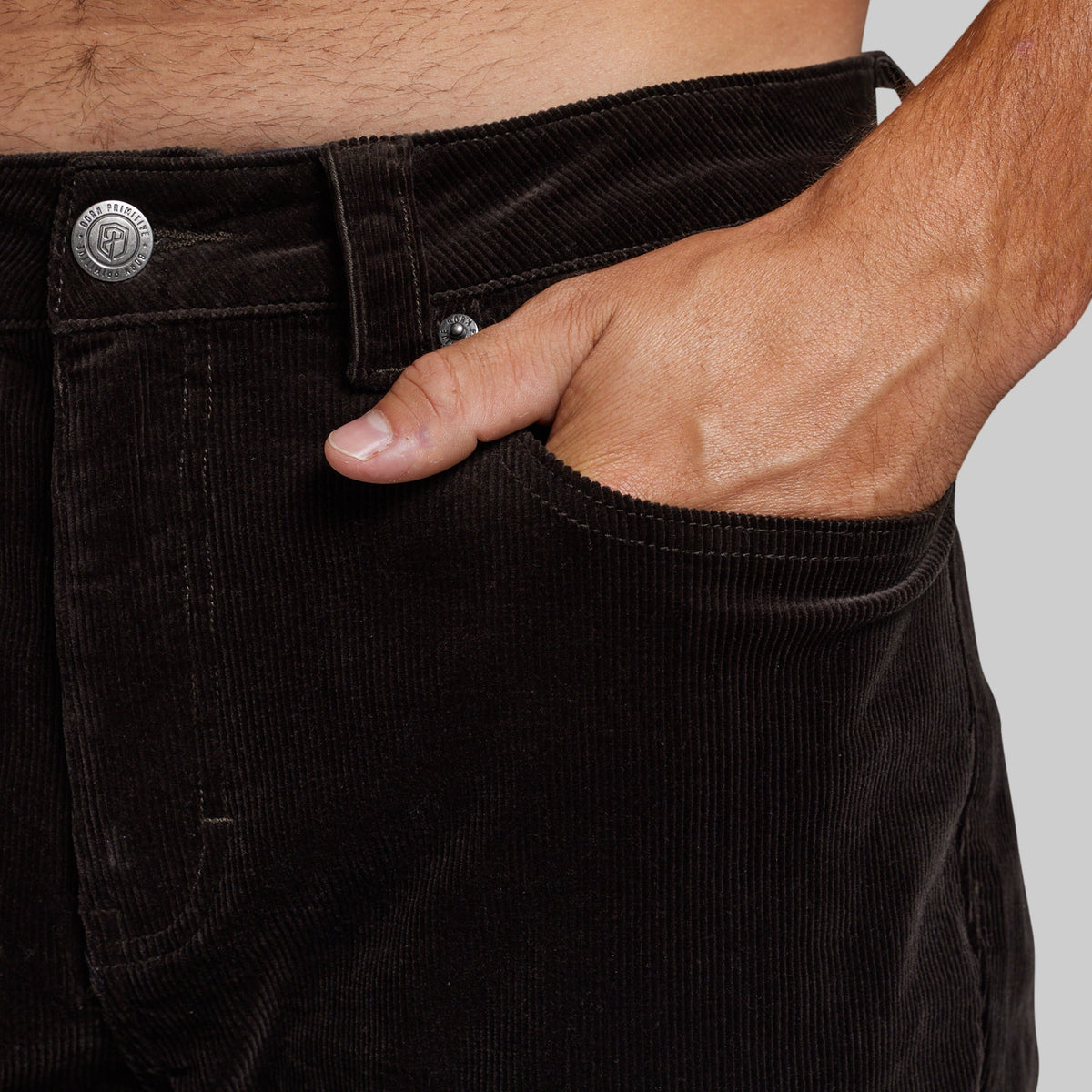 Close-up of a person wearing dark brown corduroy pants, with the hand in the front pocket and part of the waist visible.