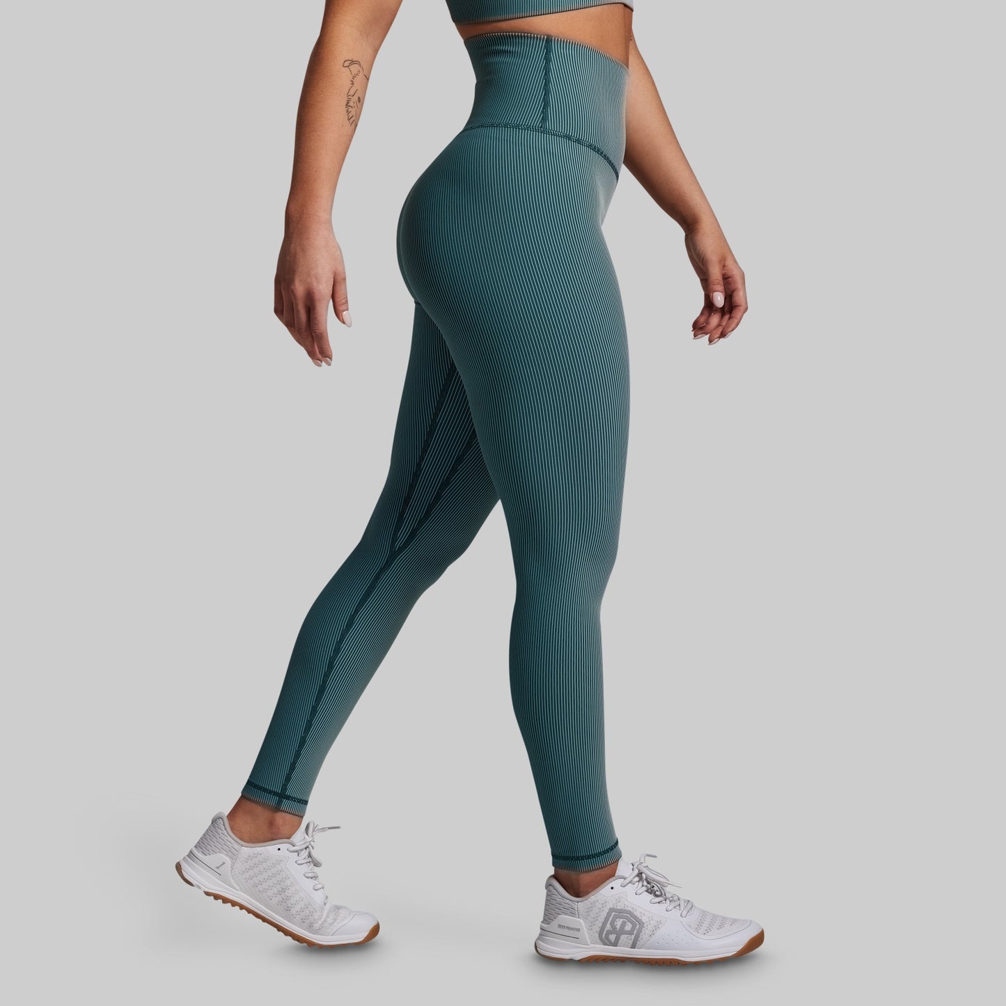 Person wearing teal ribbed leggings and white sneakers on a gray background