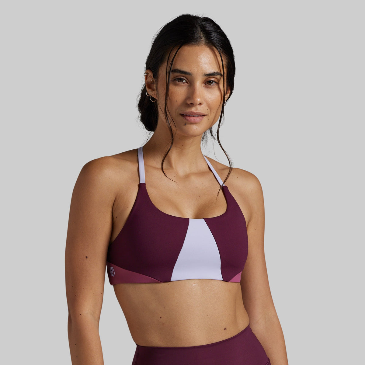 A woman modeling a color-blocked athletic sports bra in deep burgundy and white, set against a solid light gray background.