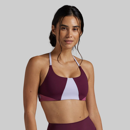A woman modeling a color-blocked athletic sports bra in deep burgundy and white, set against a solid light gray background.