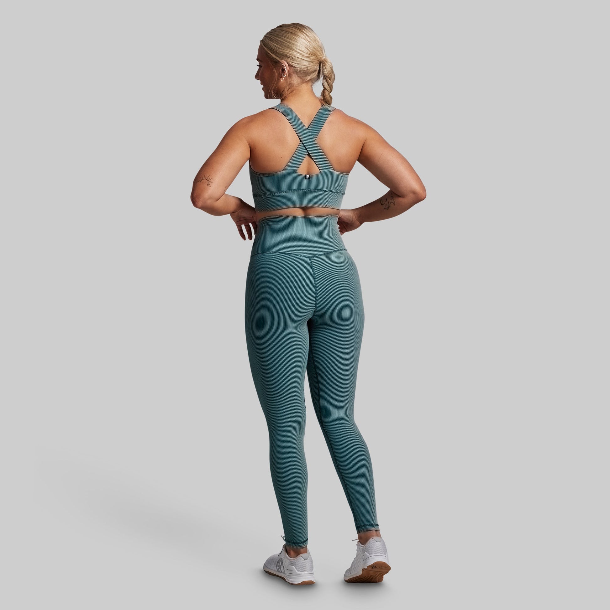 Woman wearing a teal sports bra and leggings set on a gray background