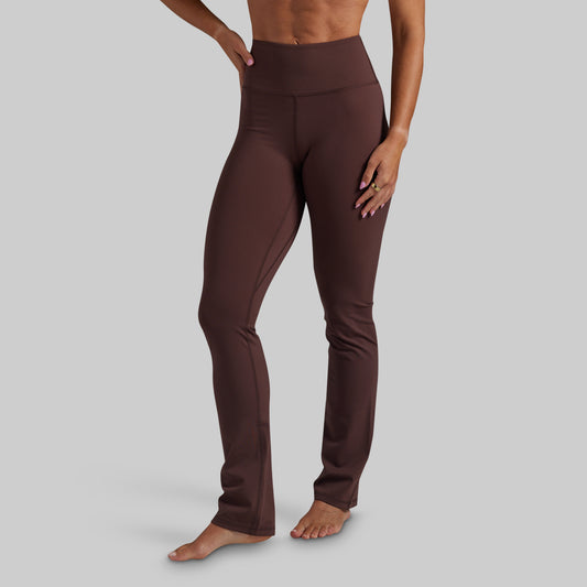 A model wearing high-waisted, full-length brown yoga pants against a solid gray background.