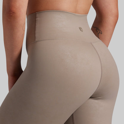 Close-up rear view of a person wearing high-waisted taupe leggings against a light gray studio background.