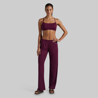 A woman modeling a matching two-piece loungewear set in deep burgundy, featuring a spaghetti-strap lounge bra and high-waisted wide-leg pants.