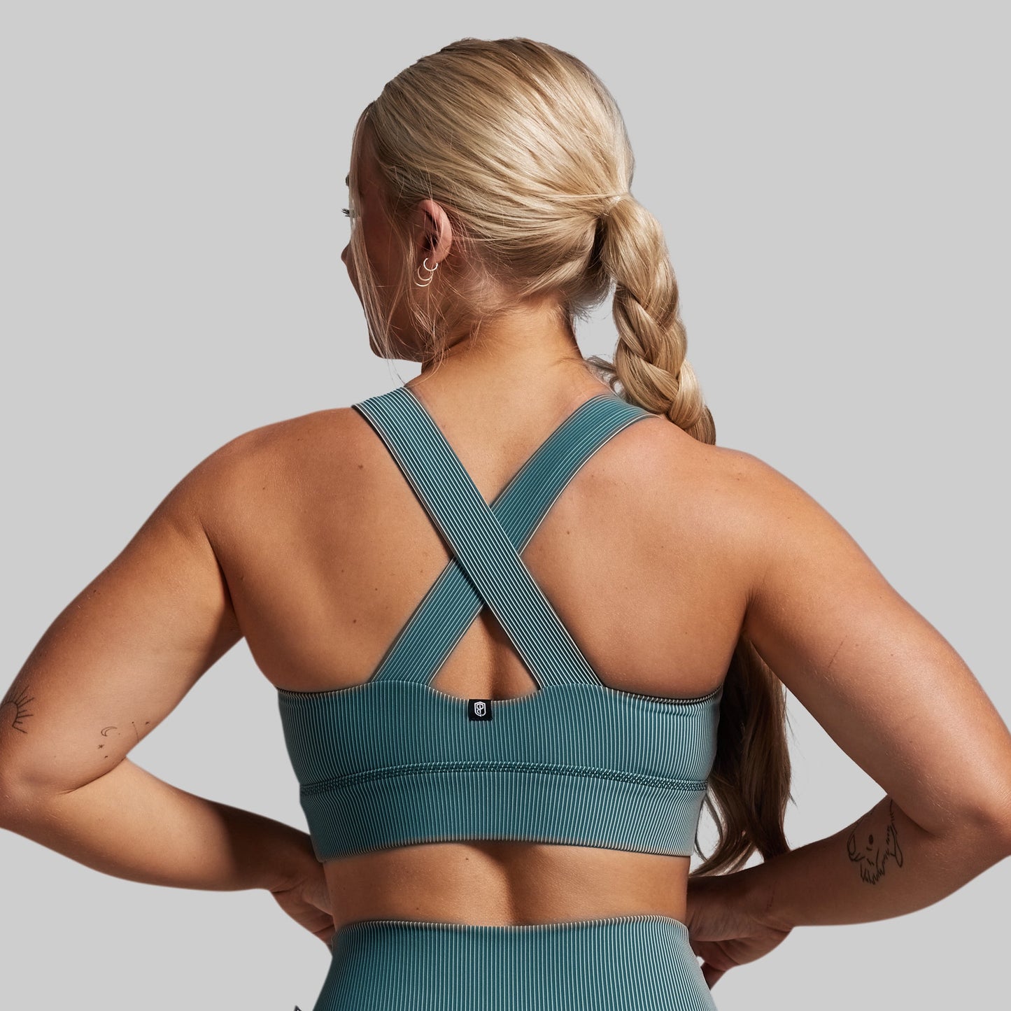 Woman wearing a teal sports bra and leggings on a gray background