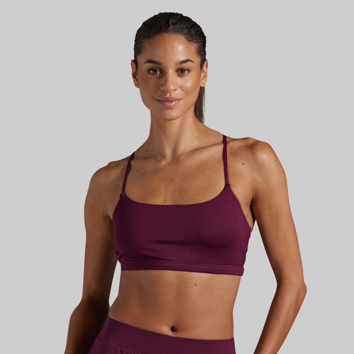 A woman modeling a deep burgundy scoop-neck lounge bra against a solid light gray background.