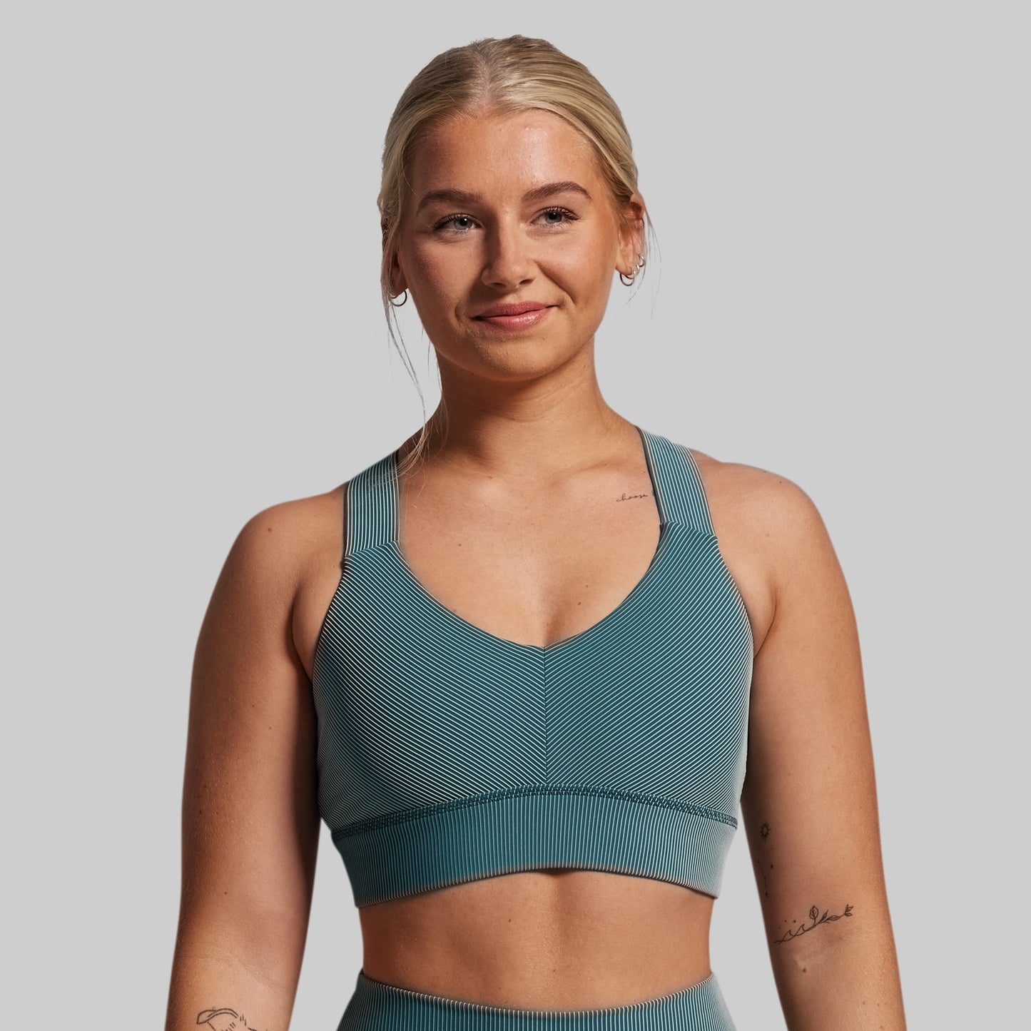 Woman wearing a teal sports bra and leggings against a plain background