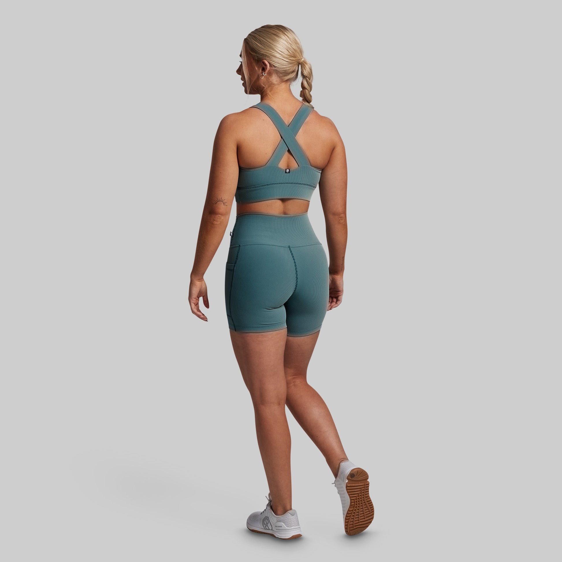 Woman wearing a green sports bra and shorts set on a gray background