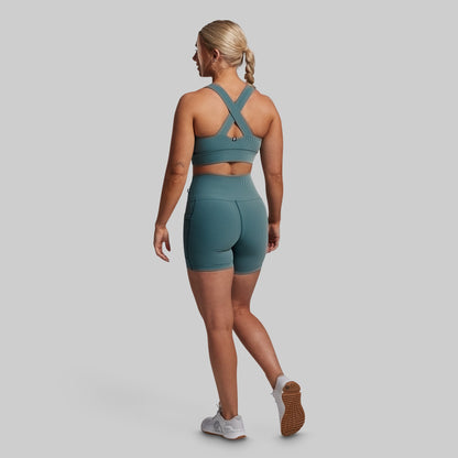 Woman wearing a green sports bra and shorts set on a gray background