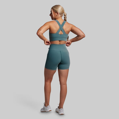 Woman wearing a green sports bra and shorts set on a gray background
