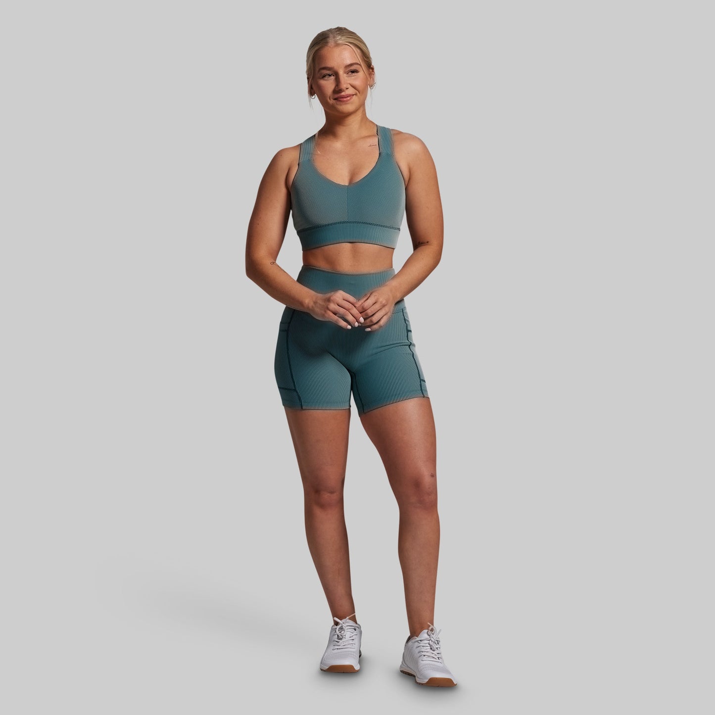 Woman wearing a green sports bra and shorts set on a gray background