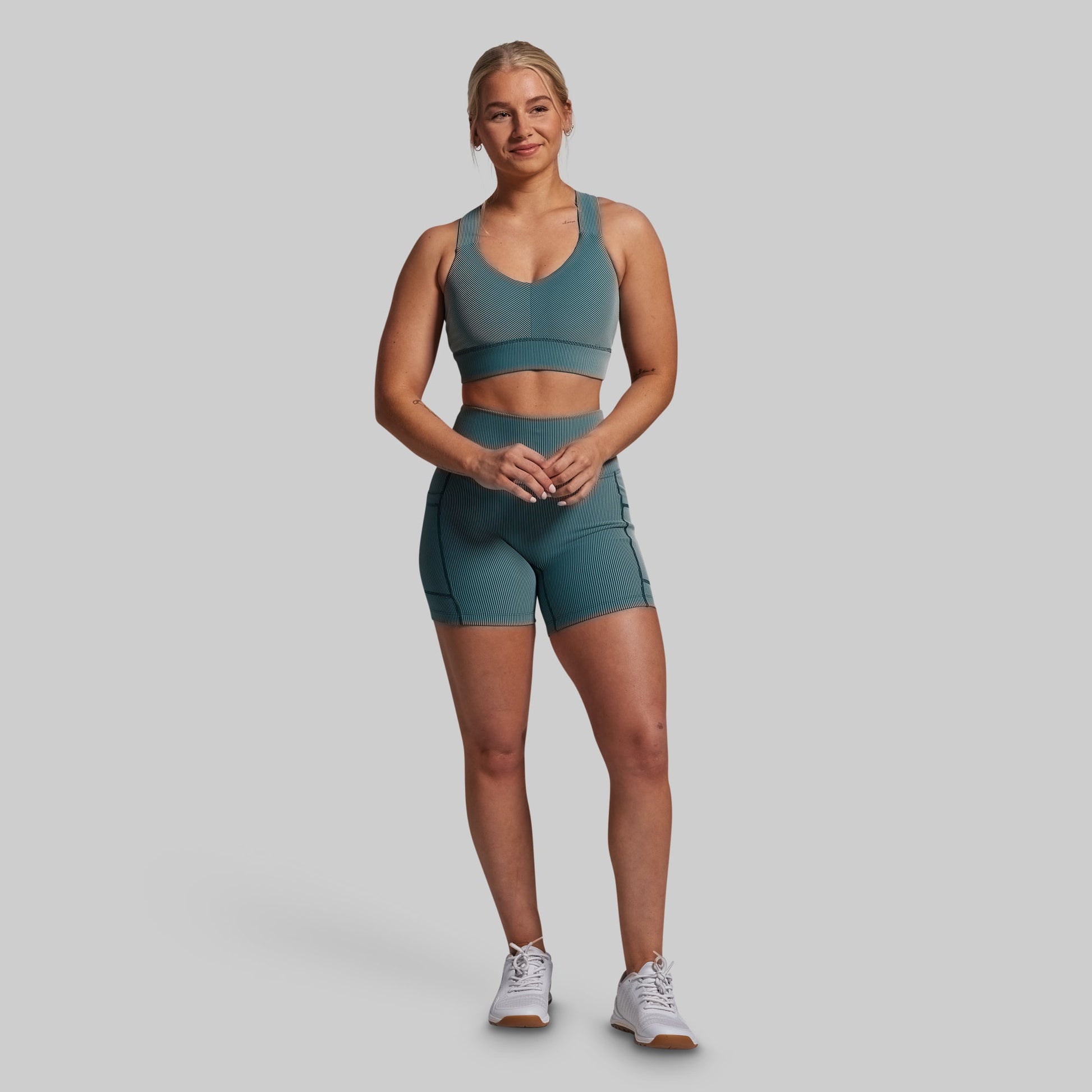 Woman wearing a green sports bra and shorts set on a gray background