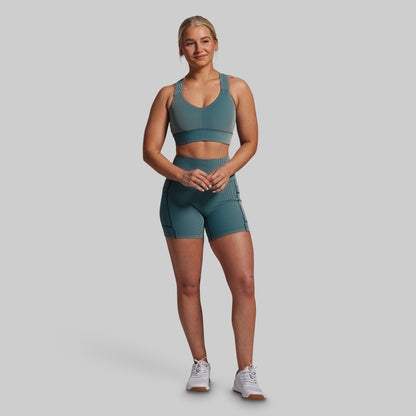 Woman wearing a green sports bra and shorts set on a gray background