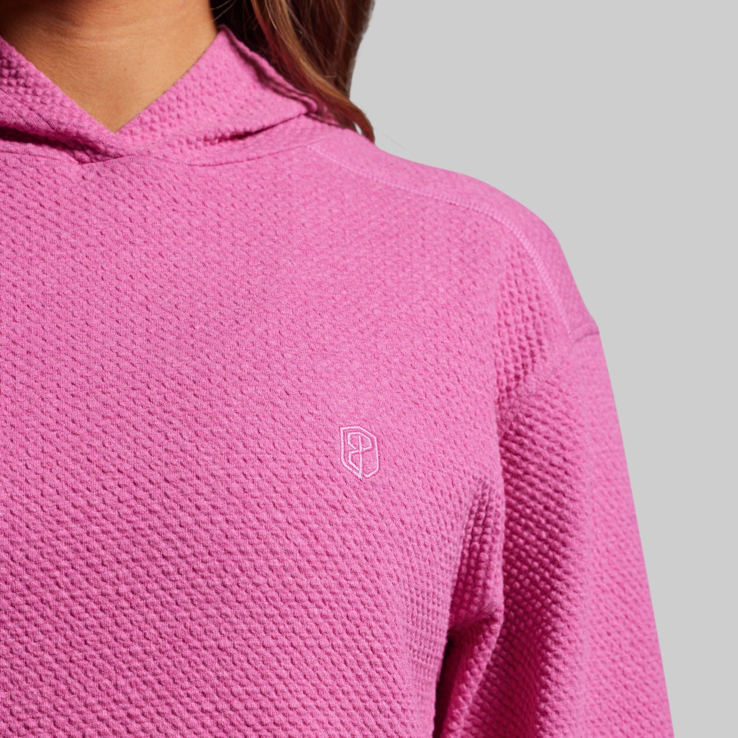 Close-up of a pink textured hoodie with a small logo on a gray background