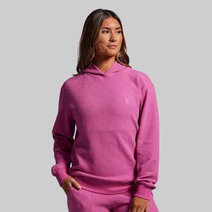 Woman wearing a pink textured hoodie and pants on a gray background