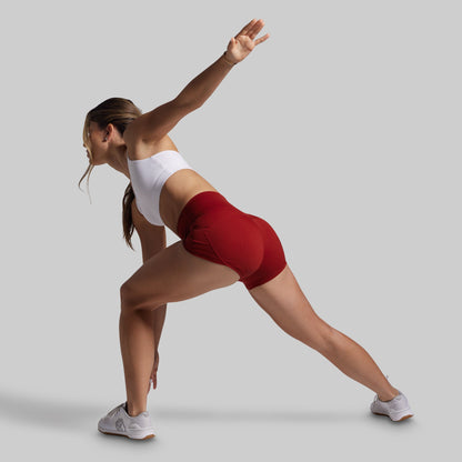 Woman in white sports bra and red shorts posing against a gray background