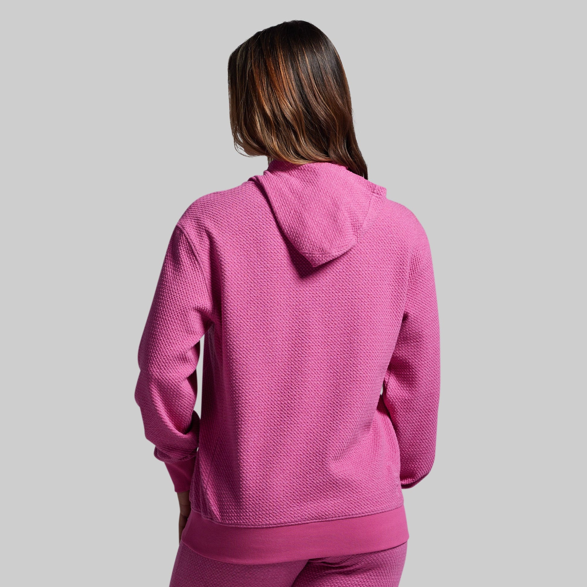 Person wearing a pink hoodie and pants on a gray background