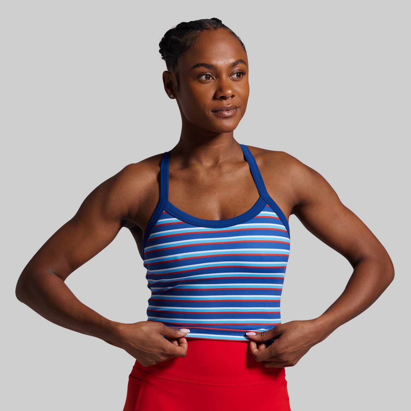 Woman wearing a blue striped sports bra and red shorts on a gray background