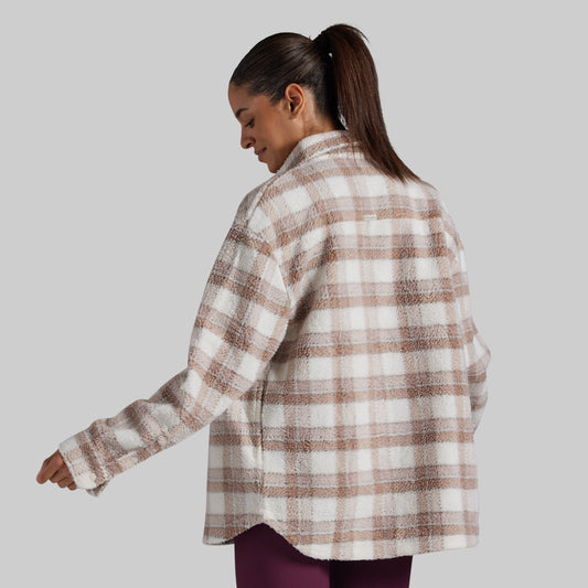 A woman wearing an oversized, long-sleeve plaid fleece button-up shirt in beige and white, shown from a three-quarters back view against a solid gray background.