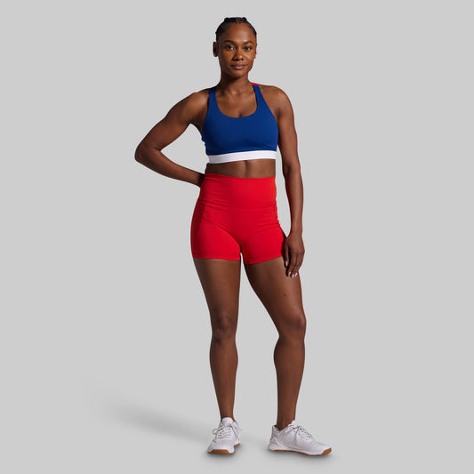 Woman wearing a blue sports bra and red shorts on a gray background