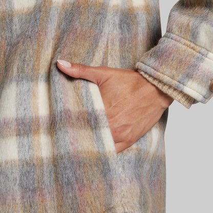 Close-up of a person wearing a fuzzy plaid coat with a hand in the pocket, showing the sleeve cuff and textured fabric against a light gray background.