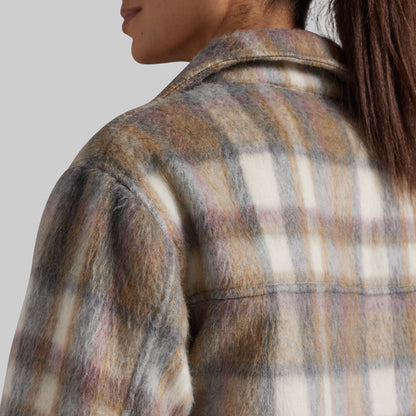 Close-up back view of a person wearing a fuzzy plaid flannel-style jacket in warm brown, cream, and muted mauve tones against a light gray studio background.