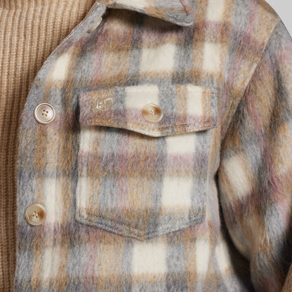 Close-up of a fuzzy plaid jacket with a chest pocket, featuring a cream, gray, and muted pink pattern, worn over a tan ribbed knit sweater.