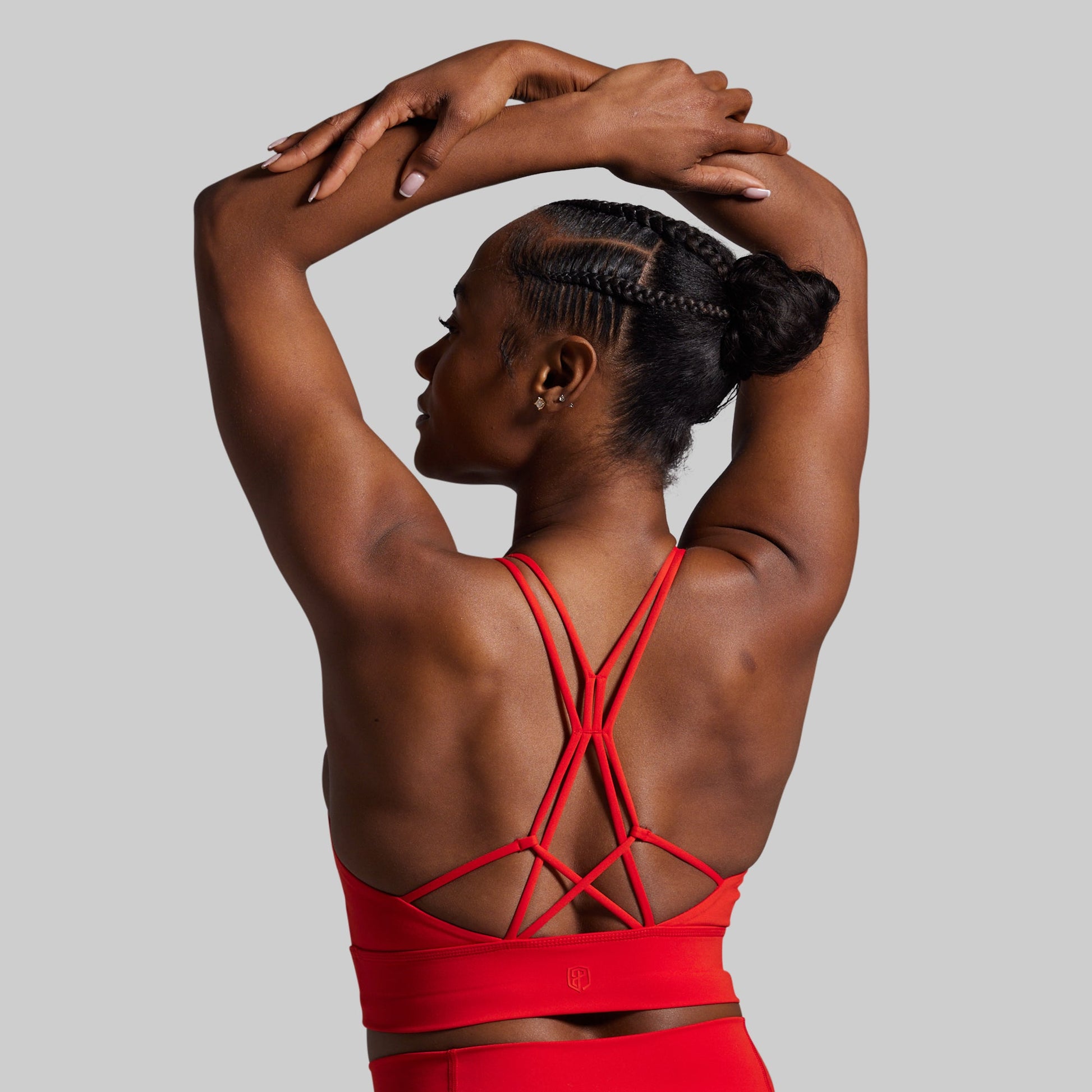 Woman wearing a red sports bra with criss-cross straps on a gray background