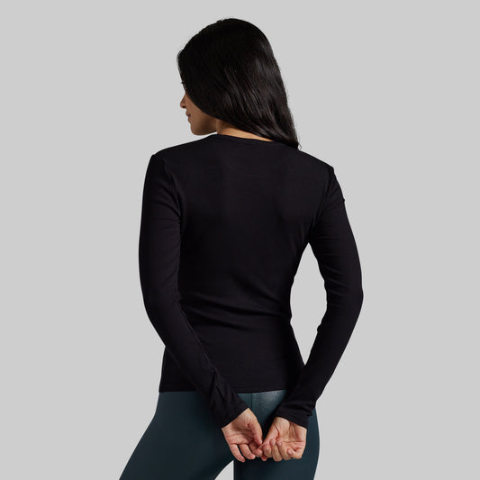 A woman shown from the back wearing a fitted black long-sleeve top and dark leggings against a plain light gray studio background.