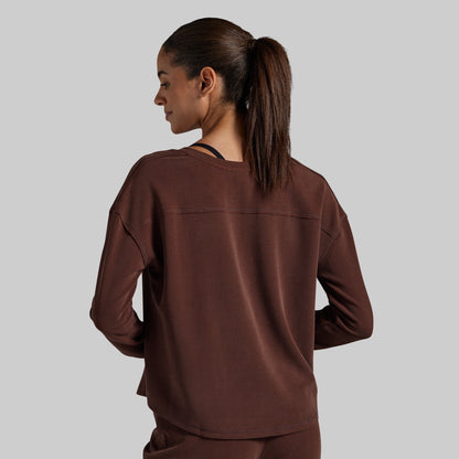 A woman is shown from the back wearing a dark brown long-sleeve top and matching pants against a solid gray background.