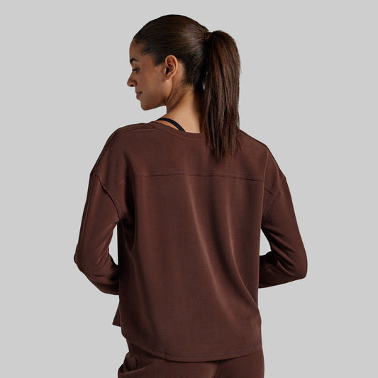 A woman is shown from the back wearing a dark brown long-sleeve top and matching pants against a solid gray background.