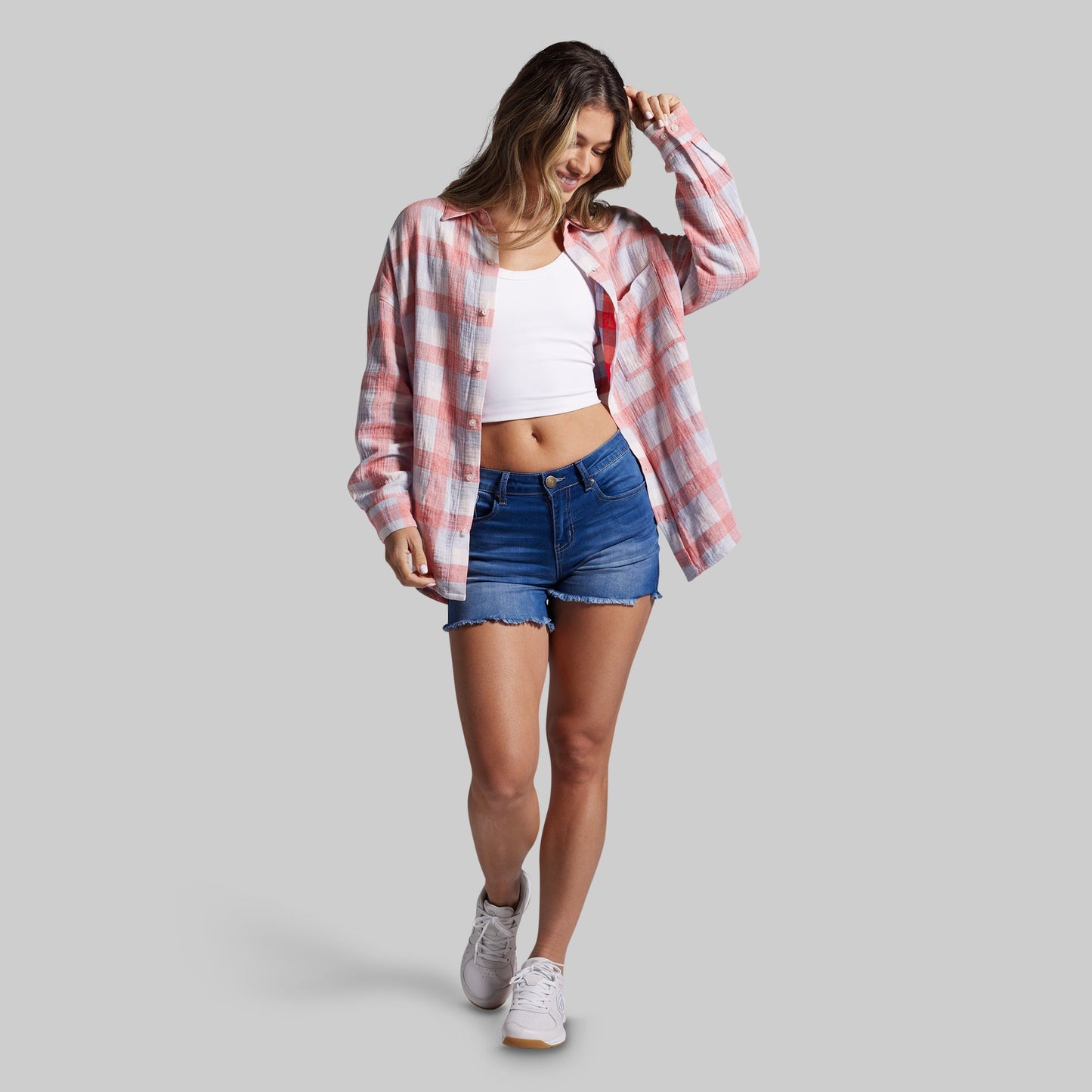 Woman wearing a plaid shirt, white top, and denim shorts on a gray background